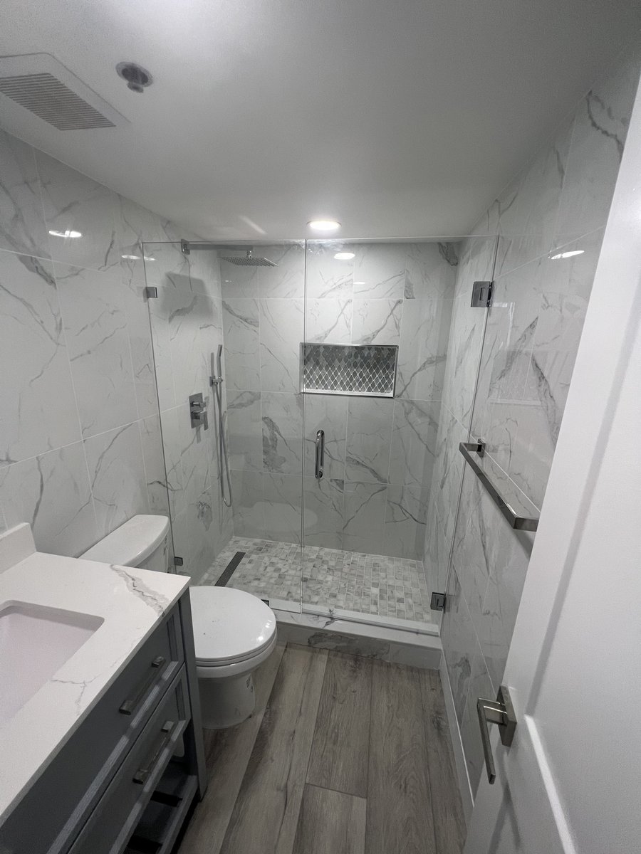 Finished bathroom remodel by KM — marble-look tile walk-in shower with glass doors, tile niche, and gray vanity