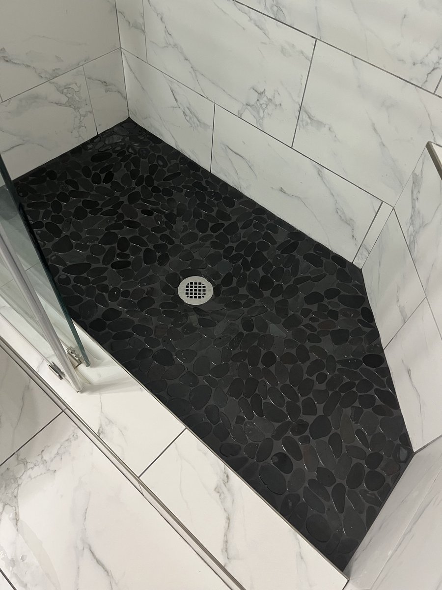 Close-up of a black pebble tile shower floor with marble-look wall tile by KM